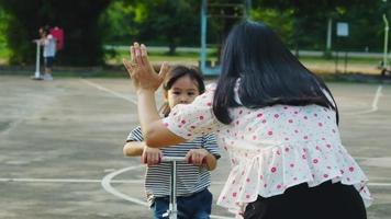 glad mamma och barn gör high five medan de åker skoter i sommarparken. barn som leker utomhus med skotrar. fritidsaktiviteter och utomhussporter för barn video