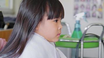 asiatisk liten flicka klipps av en frisör på en skönhetssalong. frisör gör frisyrer för söta små tjejer. söt liten flicka skär lugg. video