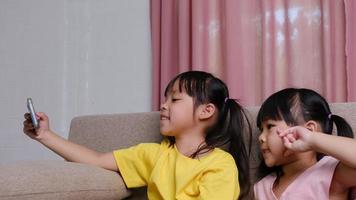 Two sisters are taking selfies on their smartphones sitting on the sofa at home. video