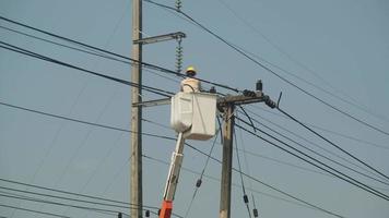 Electrician worker in lift bucket working on an electric pole to install and repair wires.