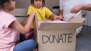 dos encantadoras hermanas con su madre poniendo su ropa en una caja de donaciones en casa para ayudar a los pobres. concepto de donación.