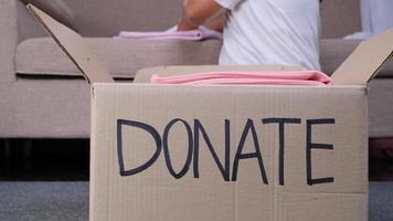 jovem mulher colocando roupas em caixa de doação em casa para ajudar os pobres. conceito de doação. video