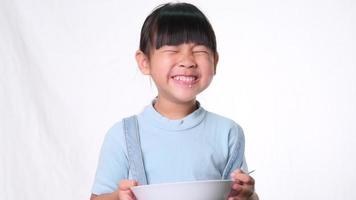 linda niña desayunando. niña feliz comiendo cereal con leche del tazón sobre fondo blanco en el estudio. nutrición saludable para los niños. video