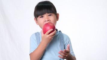 niña feliz con manzana. Linda niña asiática comiendo manzana orgánica sobre fondo blanco en el estudio. nutrición saludable para niños pequeños. video