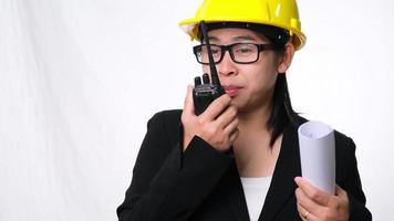 arquiteta feminina em um capacete segurando planos de construção e usando walkie-talkie e conversar com outros funcionários em um fundo branco no estúdio.