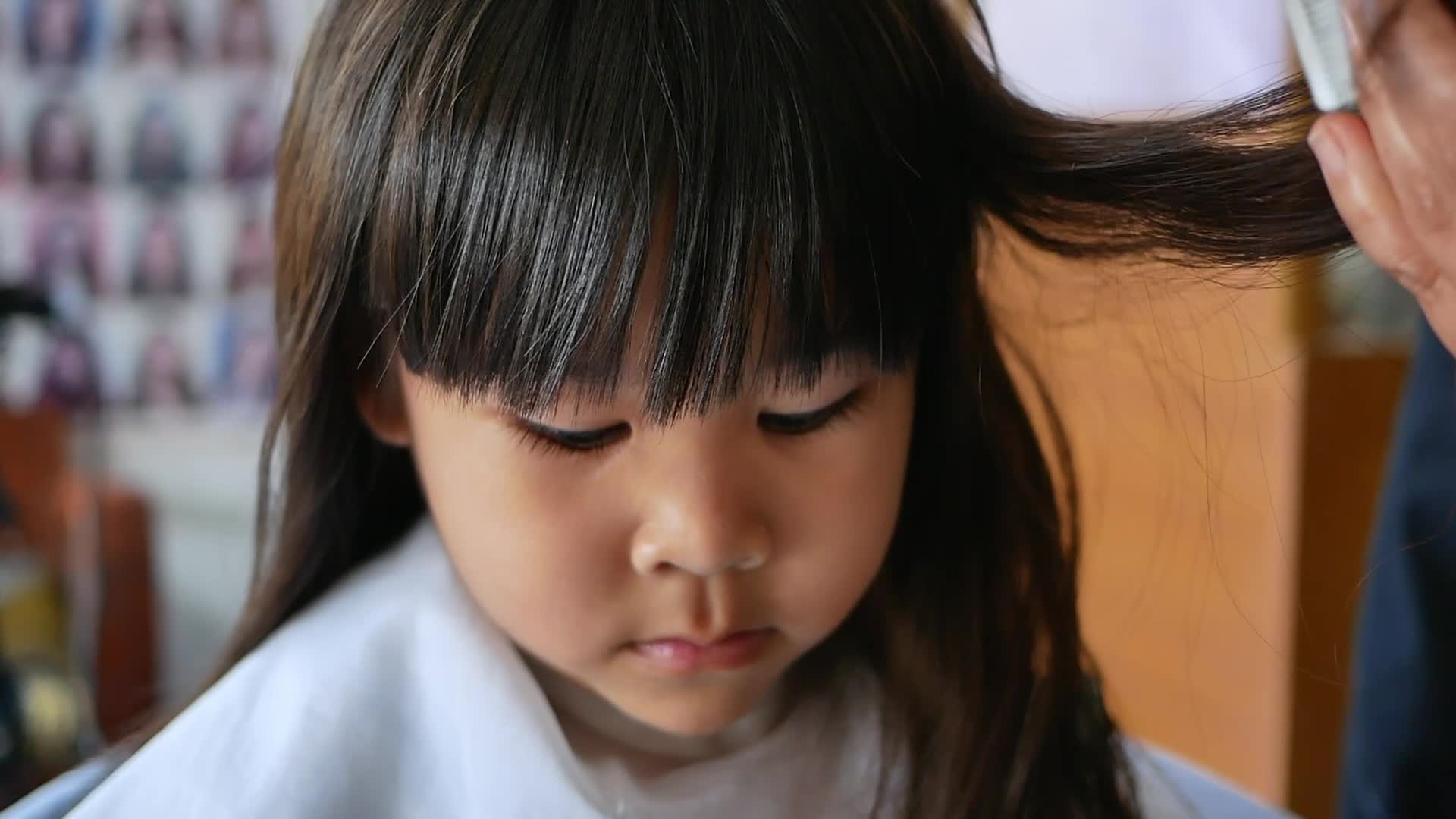 Asian little girl gets her hair cut at a beauty salon by a hairdresser.  Hairdresser makes hairstyles for cute little girls. cute little girl cutting  bangs. 6303107 Stock Video at Vecteezy
