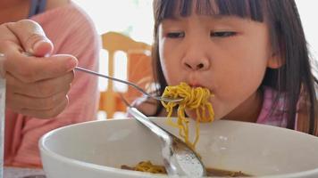 Mutter füttert ihre schöne Tochter mit thailändischen Nudeln in einem Restaurant. glückliches und gesundes kindheitskonzept video