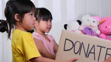 Young woman volunteer giving a donation box with lots of dolls to the children. Charitable stuffed dolls donation for kids. Donation concept. video