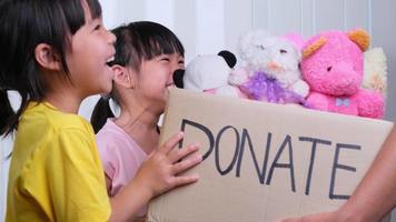 Young woman volunteer giving a donation box with lots of dolls to the children. Charitable stuffed dolls donation for kids. Donation concept. video