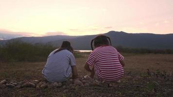 bakifrån av två småsystrar som leker med stenar vid sjön. barn tillbringar tid tillsammans med familjen på semester. video