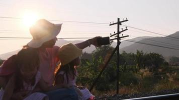 Asian mother and child sit on railroad tracks and take selfies with smartphones at sunset. video