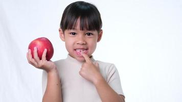 bambina felice con la mela. bambina asiatica sveglia che mangia mela organica su fondo bianco in studio. alimentazione sana per i bambini piccoli. video