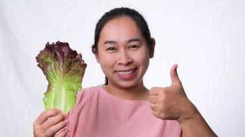 mujer asiática sana con ensalada fresca mostrando los pulgares hacia arriba sobre fondo blanco en el estudio. dieta y concepto de comida saludable.