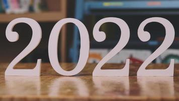 Auf einem Holztisch im Haus steht die weiße Zahl 2022. Frohes neues Jahr 2022. video