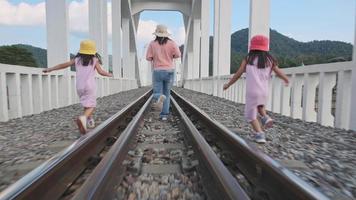 An Asian mother and daughters run together on the railroad tracks at the old white railway bridge, Tha Chompoo, a famous tourist attraction in northern Thailand. video