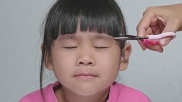 asiatisk mamma klipper sin dotters hår själv hemma. mamma klipper hår åt en söt liten flicka. stanna hemma säkert från corona virus covid-19 video