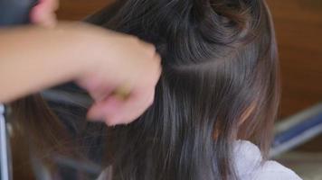 une petite fille asiatique se fait couper les cheveux dans un salon de beauté par un coiffeur. le coiffeur fait des coiffures pour de jolies petites filles. jolie petite fille coupant une frange. video