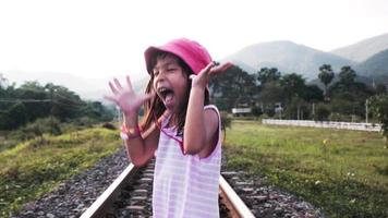 twee schattige aziatische meisjes die 's avonds samen op spoorrails op het platteland tegen de bergen rennen. video