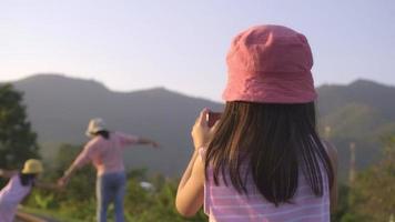 une soeur prend une photo de la mère et de la petite soeur avec un smartphone pour enregistrer des souvenirs en marchant sur les voies ferrées à la campagne contre les montagnes le soir.