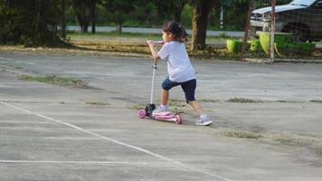 meninas bonitinhas andando de scooter na estrada no parque ao ar livre em dia de verão. garota brincando ao ar livre com scooter. lazer ativo e esporte ao ar livre para criança video