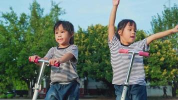Zwei süße kleine Mädchen, die am Sommertag im Freien auf der Straße im Park Roller fahren. Kinder spielen draußen mit Rollern. aktive freizeit und outdoor-sport für kinder