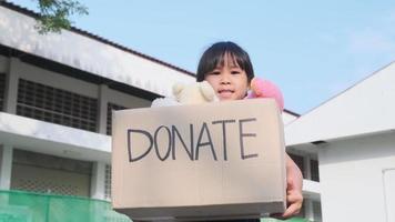 Cute little girl holding donation box with old dolls outdoors. Donation concept.