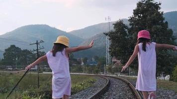 dos lindas chicas asiáticas corriendo juntas en las vías del tren en el campo contra las montañas por la noche. video