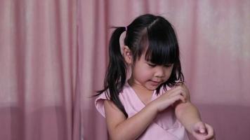 klein Aziatisch meisje jeukt en krabt haar arm binnenshuis. allergie symptomen video