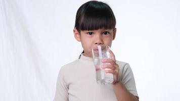 schattig klein Aziatisch meisje drinkwater uit een glas en duimen opdagen op een witte achtergrond in de studio. goede gezonde gewoonte voor kinderen. gezondheidszorg concept video