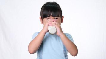 linda niña asiática bebiendo leche de un vaso y mostrando el pulgar hacia arriba sobre fondo blanco en el estudio. video