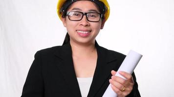 Female architect in helmet holding construction plans and smiling at camera on white background in studio. video