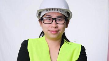 Lächelnde und selbstbewusste Ingenieurin, die einen Helm mit verschränkten Armen über einem weißen Hintergrund im Studio trägt. video
