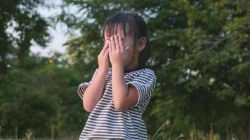 una niña asiática feliz se cubre los ojos mientras juega al escondite en el parque. familia feliz haciendo actividades juntos en vacaciones.