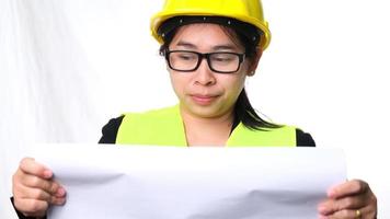 arquiteta feminina em um capacete olhando planos de construção em um fundo branco em estúdio. mulher bonita engenheira civil olhando a planta e examinando o mapa de rascunho. video