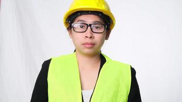 Woman technician smiling with helmet and showing a heart shape with hands on white background in studio. video
