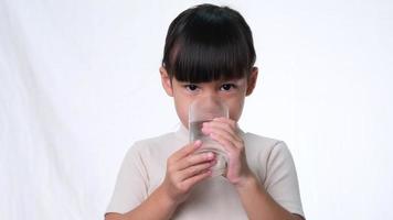 linda niña asiática bebiendo agua de un vaso sobre fondo blanco en el estudio. buen hábito saludable para los niños. concepto de salud video