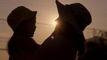 Silhouette of cute daughter hugging and kissing her loving mother at sunset at summer garden. Mother's day. video