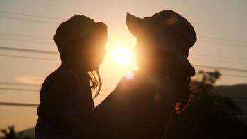 Silhouette of cute daughter hugging and kissing her loving mother at sunset at summer garden. Mother's day.