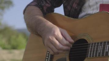 homem asiático de cabelos cacheados bonito tocando violão e cantando à beira do lago ao pôr do sol de férias. video