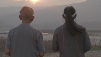 grand-père et petite-fille font du jogging au bord du lac au coucher du soleil et racontent des histoires d'expériences de vie passées. concept de mode de vie sain. video