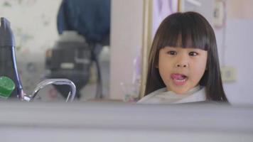 menina asiática corta o cabelo em um salão de beleza por um cabeleireiro. cabeleireiro faz penteados para meninas bonitinhas. menina bonitinha cortando franja. video