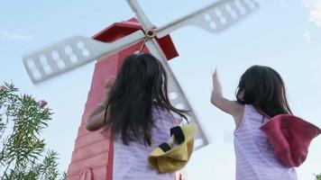 Two sisters playing with wind near windmills. Sibling girls enjoyed watching the windmills spinning in the wind.