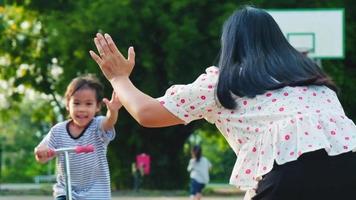 glad mamma och barn gör high five medan de åker skoter i sommarparken. barn som leker utomhus med skotrar. fritidsaktiviteter och utomhussporter för barn video