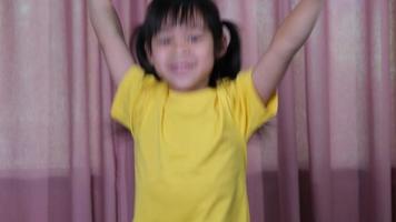 Portrait of a cute little girl in a yellow t-shirt jumping happily at home. Active girls feel freedom. Concept of facial expressions and gestures