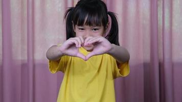 Cute little girl making heart gestures with hands showing love and care. Healthy smiling girl showing love symbol.