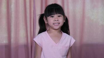 retrato de una niña sonriente feliz sobre un fondo de cortina rosa en casa. video
