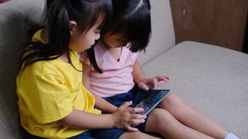 dos hermanas están jugando juegos en línea en teléfonos inteligentes sentados en el sofá de casa. concepto moderno de comunicación y adicción a los gadgets. video