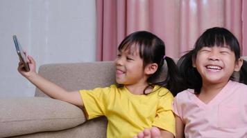 Two sisters are taking selfies on their smartphones sitting on the sofa at home. video