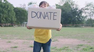 schattig klein meisje met donatiedoos met oude poppen buitenshuis. donatie concept. video
