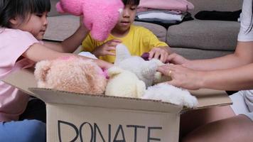 deux adorables sœurs avec sa mère mettant ses vêtements dans une boîte de dons à la maison pour aider les pauvres. notion de don. video